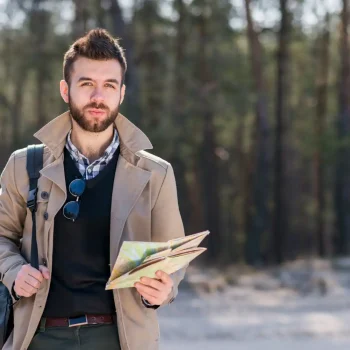 portrait-male-traveler-with-his-backpack-shoulder-holding-map-hand-looking-camera